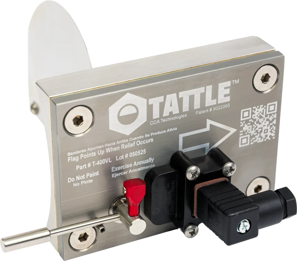A close-up of a Tattle brand industrial safety device with a metal plate, red flag indicator, black sensor, and engraved instructions, including a QR code and patent number.